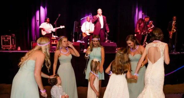 A live band performing on stage at a wedding reception with a bride and guests dancing in the foreground.