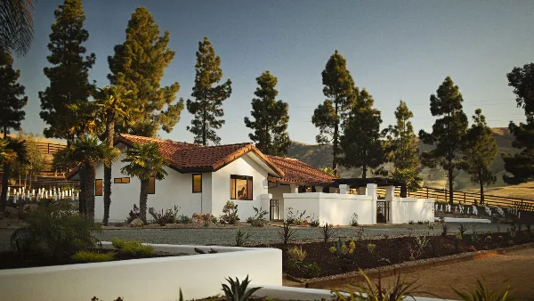 Exterior view of the white Spanish-style La Lomita Ranch estate with red tile roof, surrounded by palm trees and rolling hills.