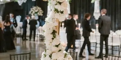Luxury wedding reception table with white floral centerpiece, candles, and chandeliers in a ballroom.