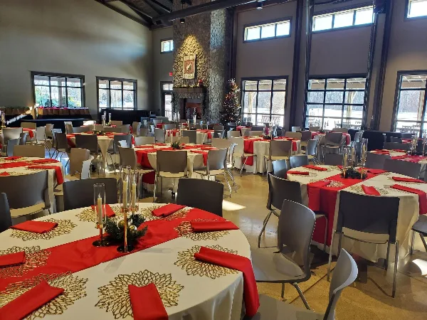 An indoor event space with round tables set with white tablecloths, red runners, and chairs, ready for a party or wedding.