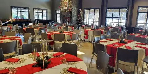 An indoor event space with round tables set with white tablecloths, red runners, and chairs, ready for a party or wedding.
