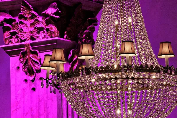 Interior view of a wedding venue featuring a large crystal chandelier and ornate architectural details illuminated by purple lighting.