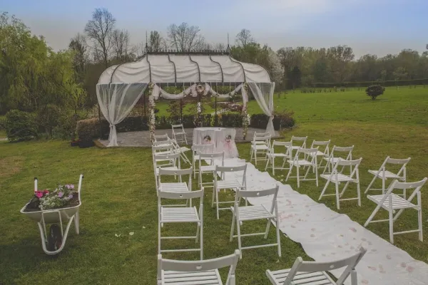 An outdoor wedding ceremony setup featuring a white canopy tent, rows of white folding chairs, and a floral aisle runner on a grassy lawn.