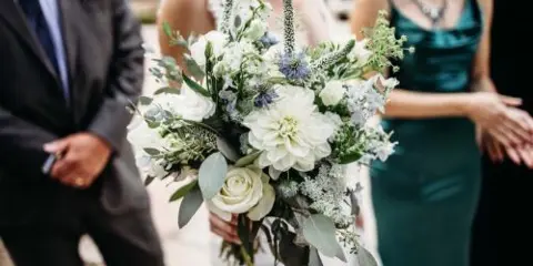 A bride holding a white and green floral bouquet during a wedding ceremony.