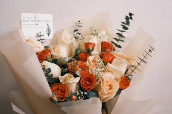 A wrapped bouquet of orange and cream roses with eucalyptus stems.