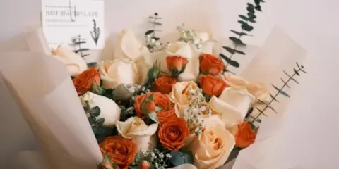 A wrapped bouquet of orange and cream roses with eucalyptus stems.