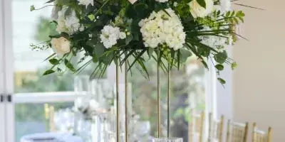 A tall, lush floral centerpiece featuring white hydrangeas and pink roses on a gold stand, set on a decorated wedding table.