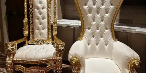 Two ornate gold and white throne chairs with tufted upholstery and decorative gold frames.