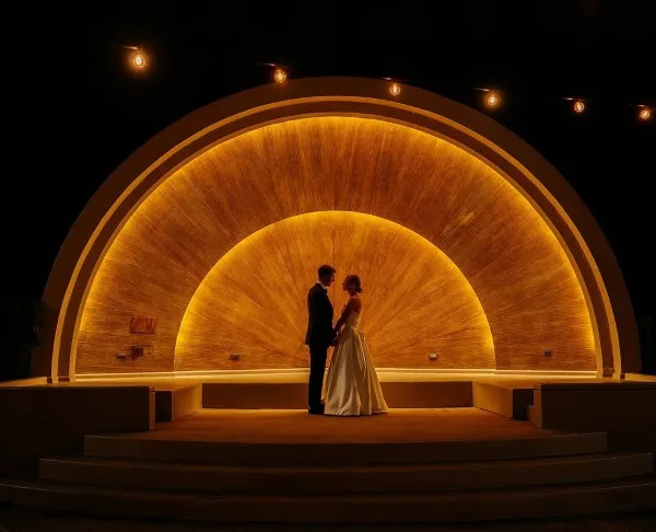 A bride and groom standing together in front of a large, illuminated golden archway at night.