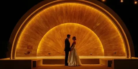 A bride and groom standing together in front of a large, illuminated golden archway at night.