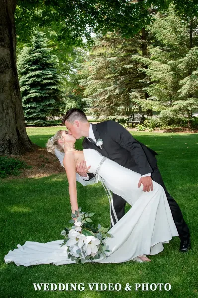 A bride and groom sharing a kiss in a dip pose on a grassy lawn with trees in the background.