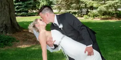 A bride and groom sharing a kiss in a dip pose on a grassy lawn with trees in the background.