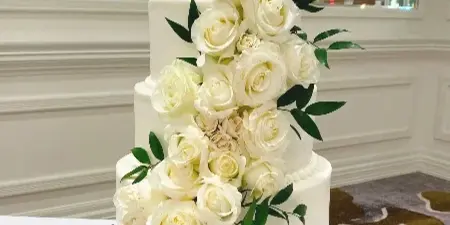 A four-tier white wedding cake decorated with cascading white roses and green leaves.