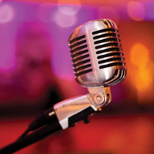 A close-up of a silver vintage microphone on a stand with a blurred, colorful background.