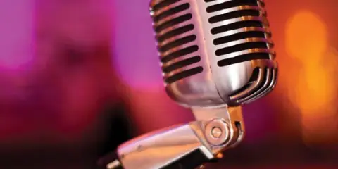 A close-up of a silver vintage microphone on a stand with a blurred, colorful background.