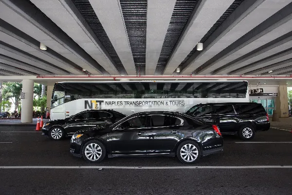 A fleet of luxury vehicles including a motor coach, limousine, and sedans parked at an airport terminal.
