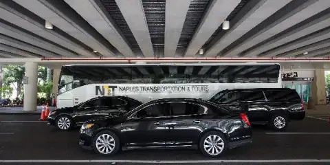 A fleet of luxury vehicles including a motor coach, limousine, and sedans parked at an airport terminal.