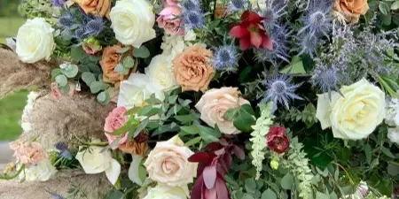 A tall, artistic floral arrangement featuring roses, pampas grass, and greenery in a white vase.