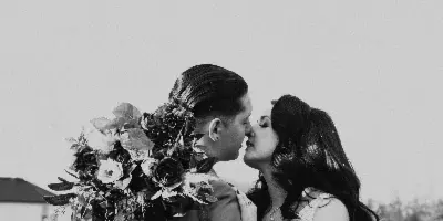 Black and white photograph of a couple in wedding attire kissing in a field of flowers.