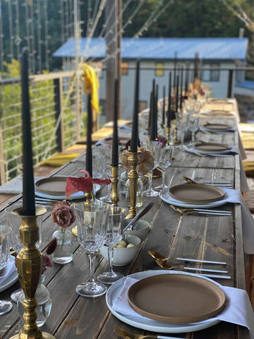 A long wooden table set for a wedding reception with plates, glassware, and tall black candles.