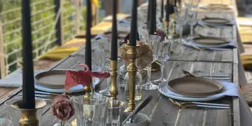 A long wooden table set for a wedding reception with plates, glassware, and tall black candles.