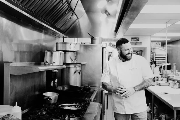 A professional chef in a white uniform standing in a commercial kitchen with stainless steel equipment.
