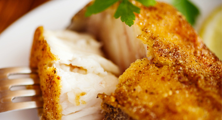 A close-up of a plated fried catfish fillet garnished with parsley and a lemon wedge.