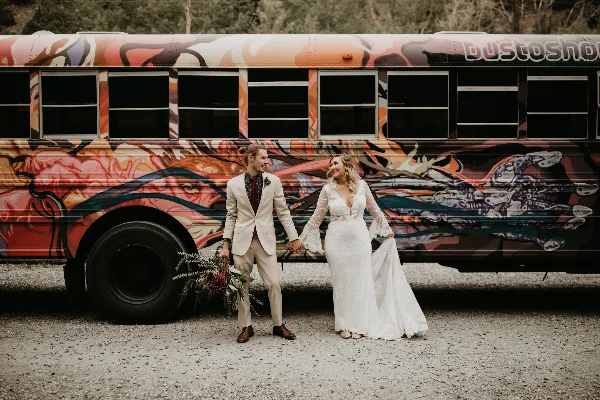 A bride and groom standing together in front of a vibrantly painted bus.