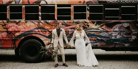 A bride and groom standing together in front of a vibrantly painted bus.