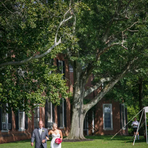 A bride and groom walking on the lawn in front of a red brick historic mansion.