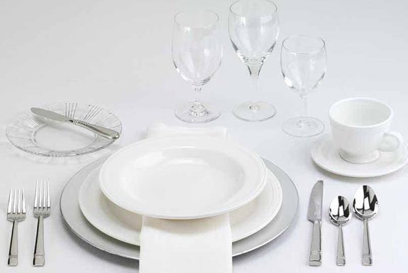 A formal table setting featuring white plates, silver cutlery, and glassware.