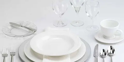 A formal table setting featuring white plates, silver cutlery, and glassware.