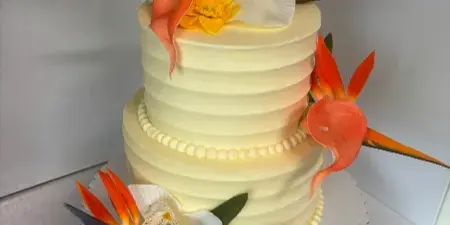 A two-tier white wedding cake decorated with tropical flowers and a gold Mr & Mrs topper.