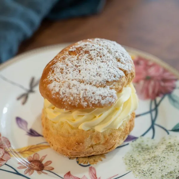 A cream puff filled with vanilla cream and dusted with powdered sugar on a floral plate.