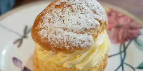 A cream puff filled with vanilla cream and dusted with powdered sugar on a floral plate.