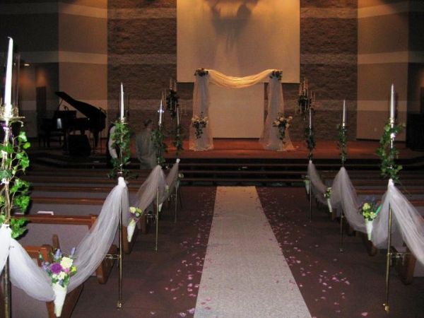 Interior of a wedding chapel with a decorated aisle, floral arrangements, and a stage set up for a ceremony.