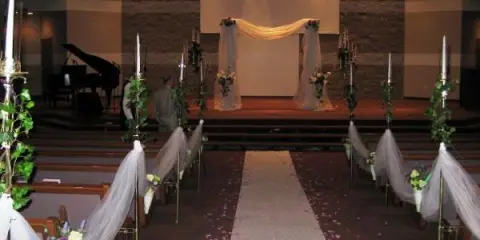 Interior of a wedding chapel with a decorated aisle, floral arrangements, and a stage set up for a ceremony.