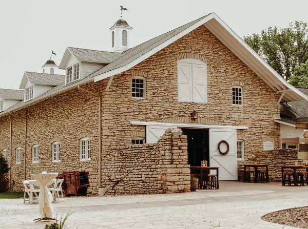Exterior view of the Mayowood Stone Barn venue featuring a large stone building with white cupolas and outdoor event tables.