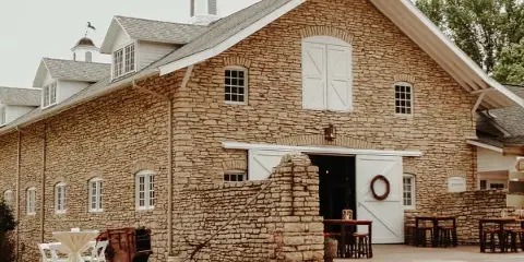 Exterior view of the Mayowood Stone Barn venue featuring a large stone building with white cupolas and outdoor event tables.