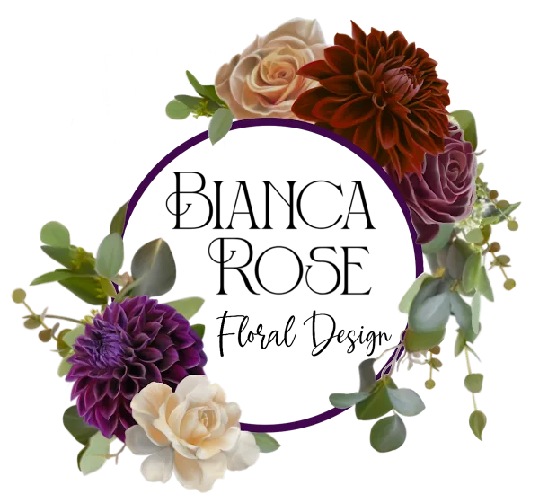 A floral arrangement featuring cream and purple roses, a purple dahlia, and a rust-colored dahlia arranged around a purple circular frame.