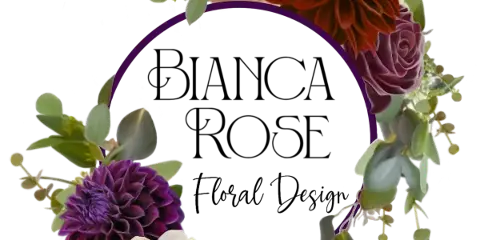 A floral arrangement featuring cream and purple roses, a purple dahlia, and a rust-colored dahlia arranged around a purple circular frame.