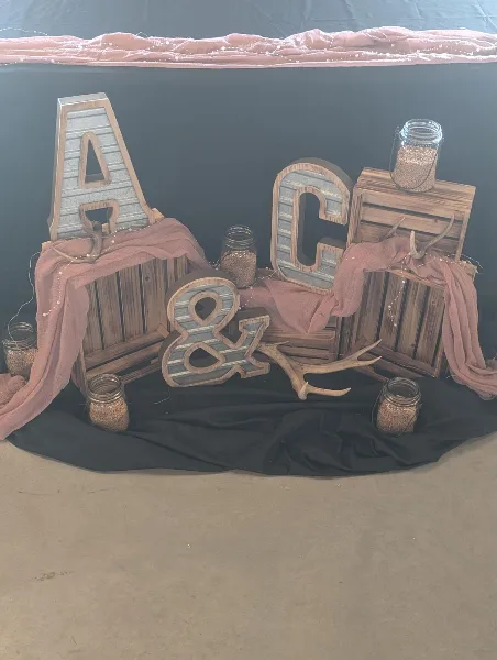 A wedding decor display featuring wooden crates, marquee letters, antlers, and mason jars on a black backdrop.