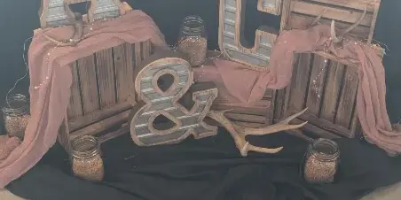 A wedding decor display featuring wooden crates, marquee letters, antlers, and mason jars on a black backdrop.
