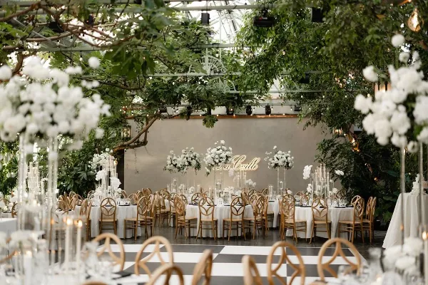 Luxury wedding reception venue featuring a lush greenery ceiling and tall white floral centerpieces on tables.