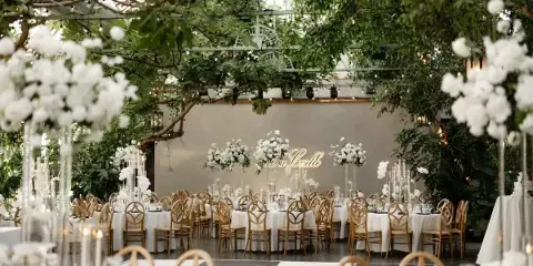Luxury wedding reception venue featuring a lush greenery ceiling and tall white floral centerpieces on tables.