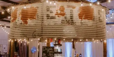 Interior view of a rustic wedding venue bar made from a corrugated metal silo with string lights and a drink menu.