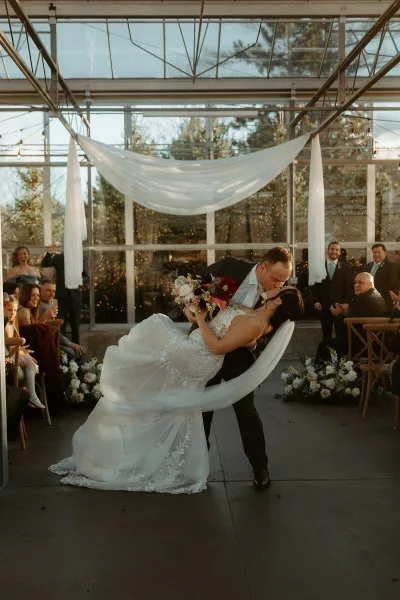 A bride and groom dancing during their wedding reception in a glass-walled venue with guests watching.