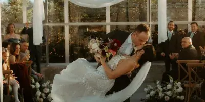 A bride and groom dancing during their wedding reception in a glass-walled venue with guests watching.