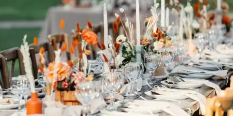 A close-up view of a long event table set with white linens, glassware, and floral centerpieces.