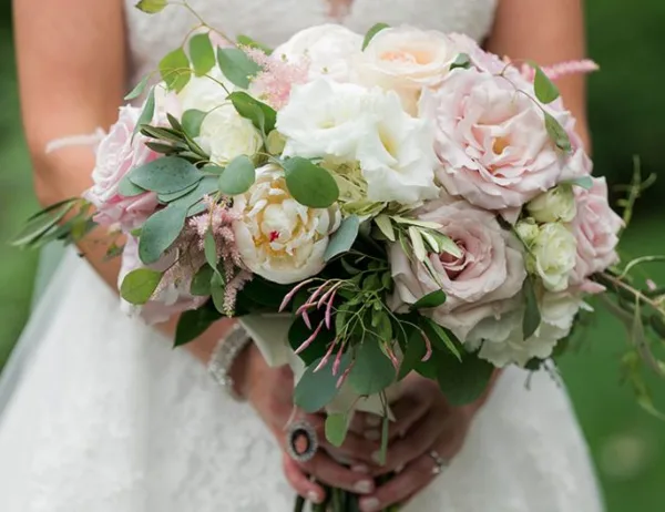 Bride holding a round wedding bouquet of white and blush roses with eucalyptus and pink filler flowers.